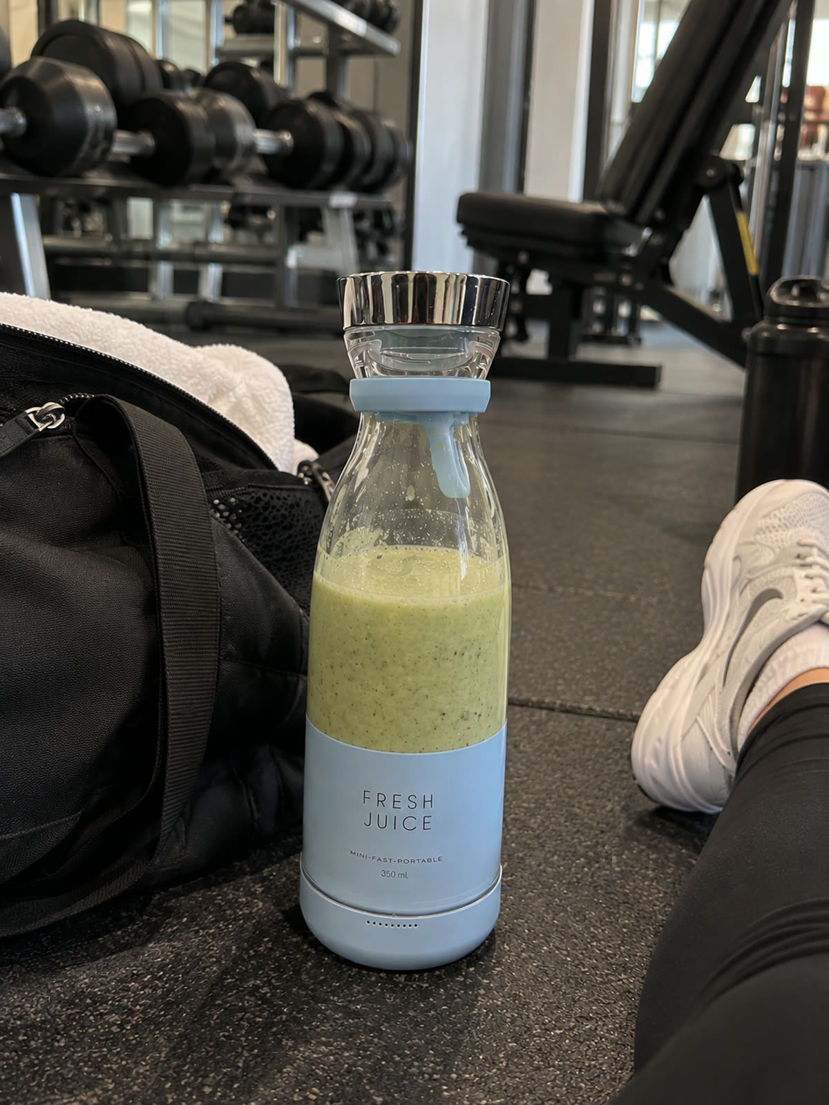 Blender portable bleu ciel rempli d'un smoothie vert posé au sol à la salle de sport