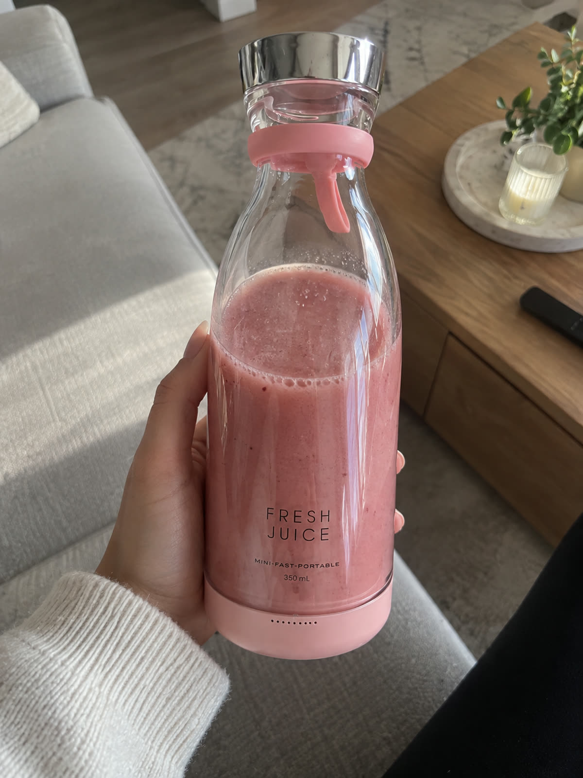 Main tenant un blender portable rose rempli d'un smoothie aux fruits rouges dans un salon
