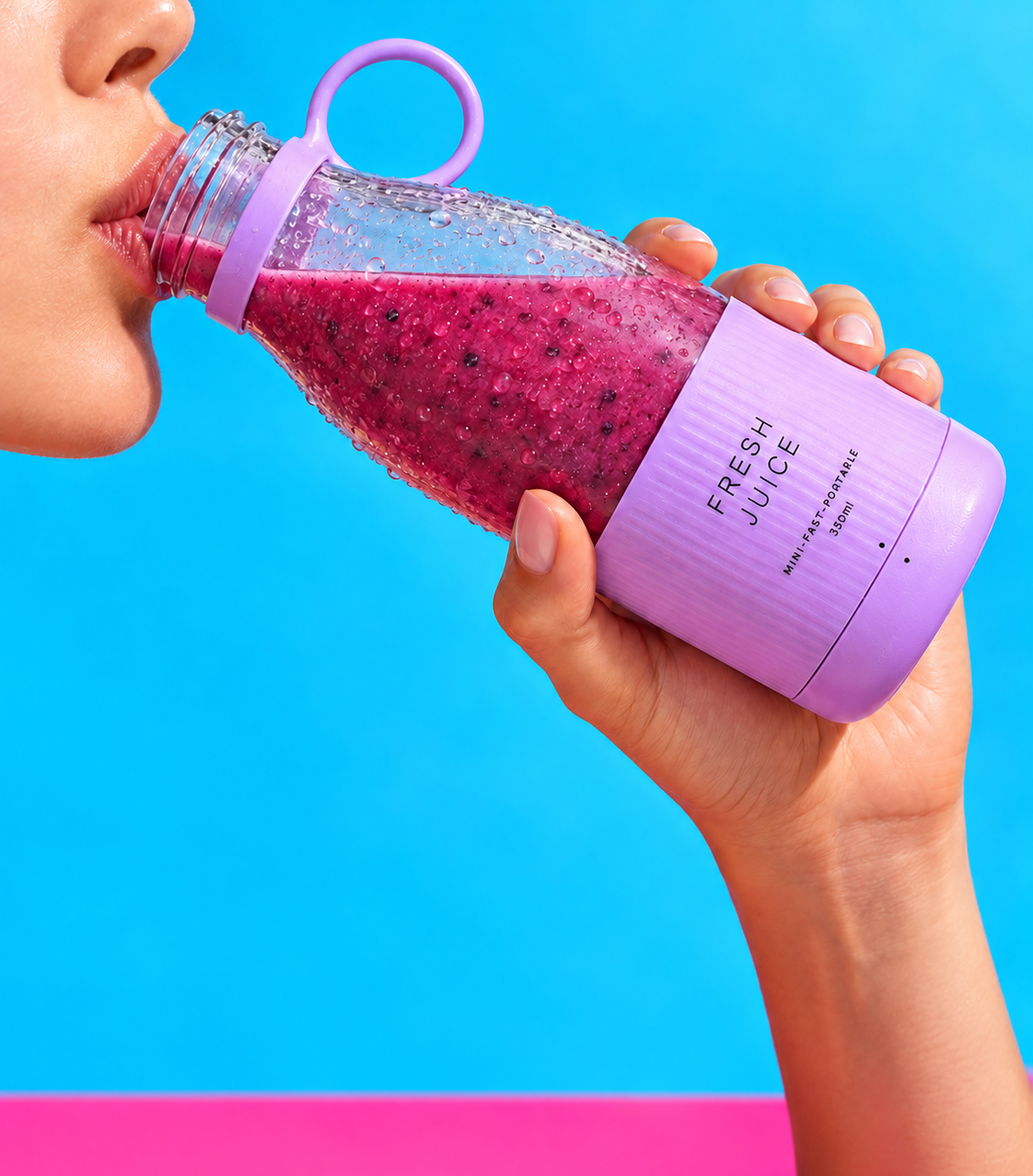 Main tenant un blender FRESHJUICE™ lavande rempli d'un smoothie rose sur fond bleu