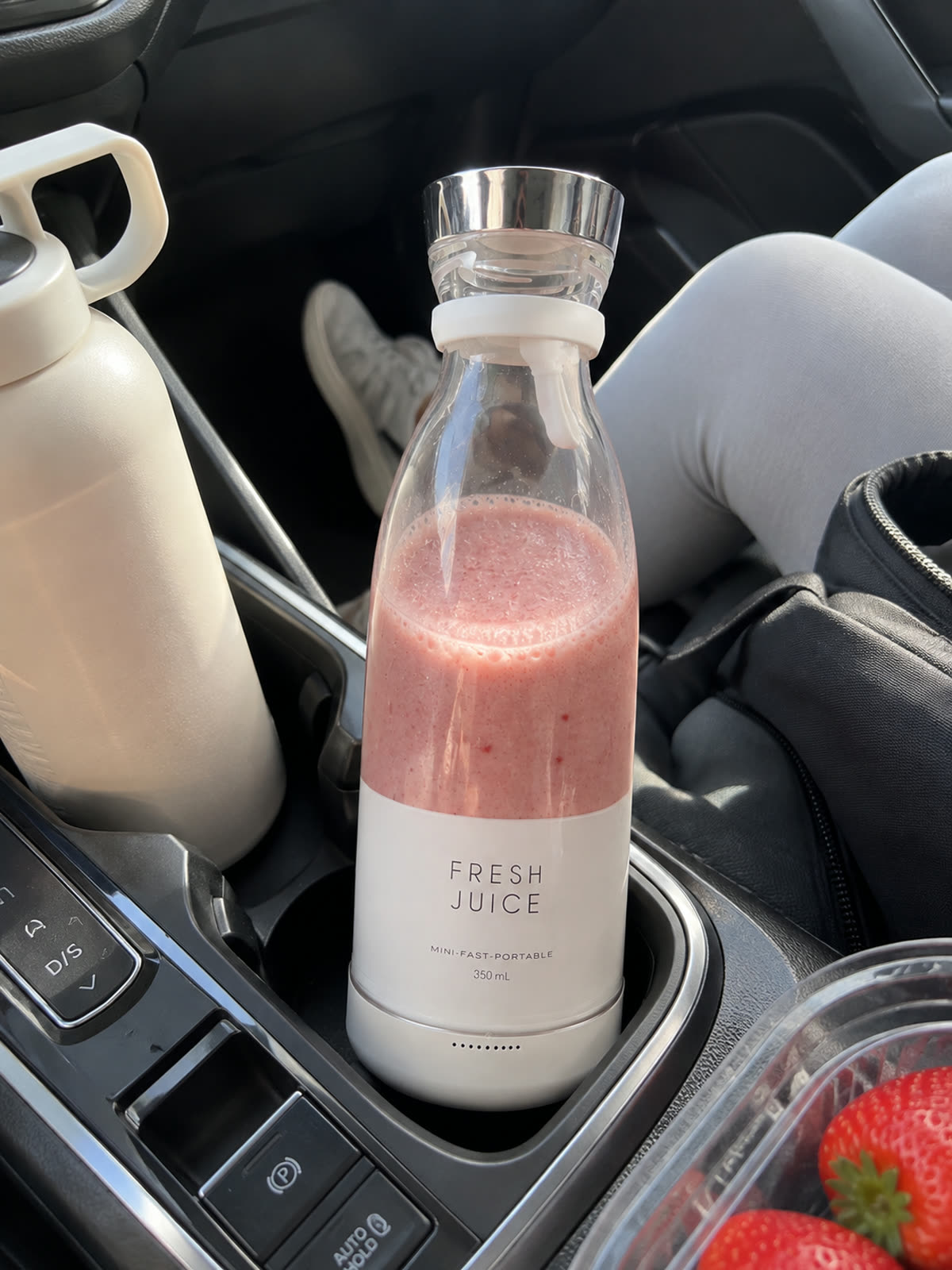 Blender portable blanc avec un smoothie rose posé dans le porte-gobelet d'une voiture